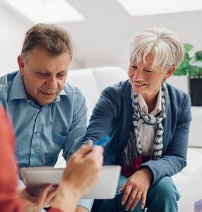 Mature Couple Meeting with Financial Advisor, selective focus to senior man and mature woman listening to financial advisor. She is pointing with index finger to digital tablet.